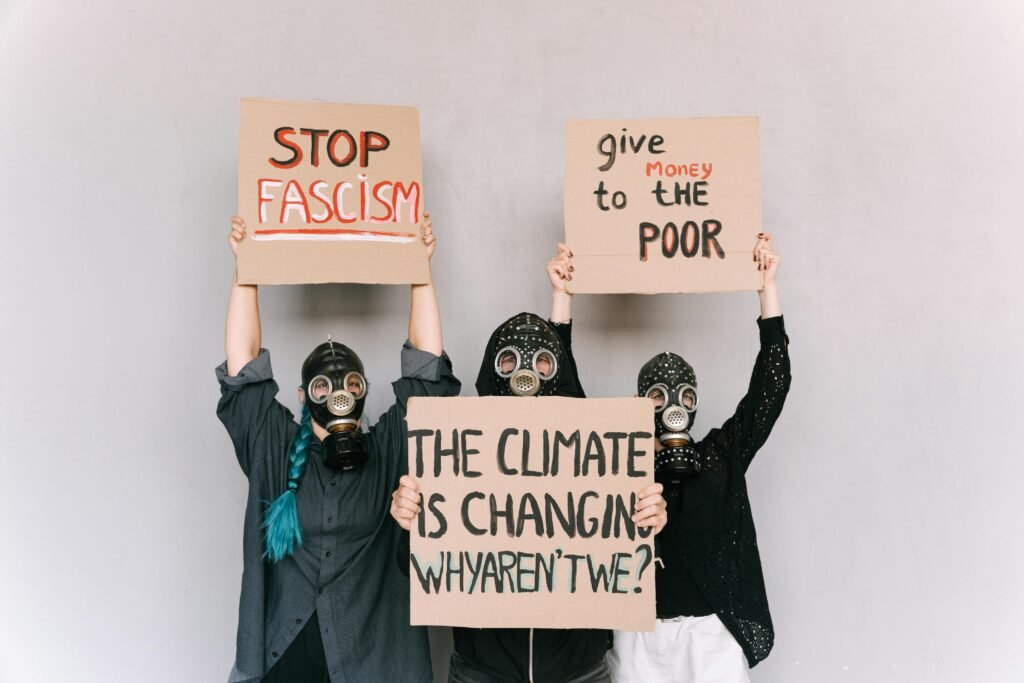 Three people wearing gas masks hold signs advocating social change and awareness.