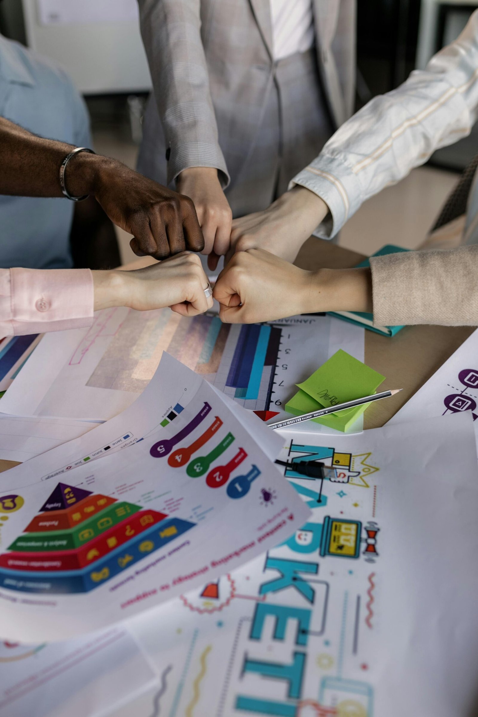 A group collaborates with a fist bump over colorful marketing charts, showcasing teamwork.