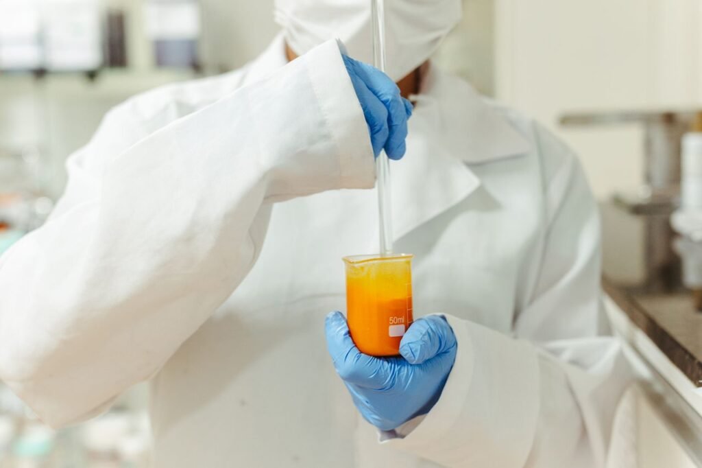 Close-up of a scientist in a lab coat mixing orange liquid in a beaker.