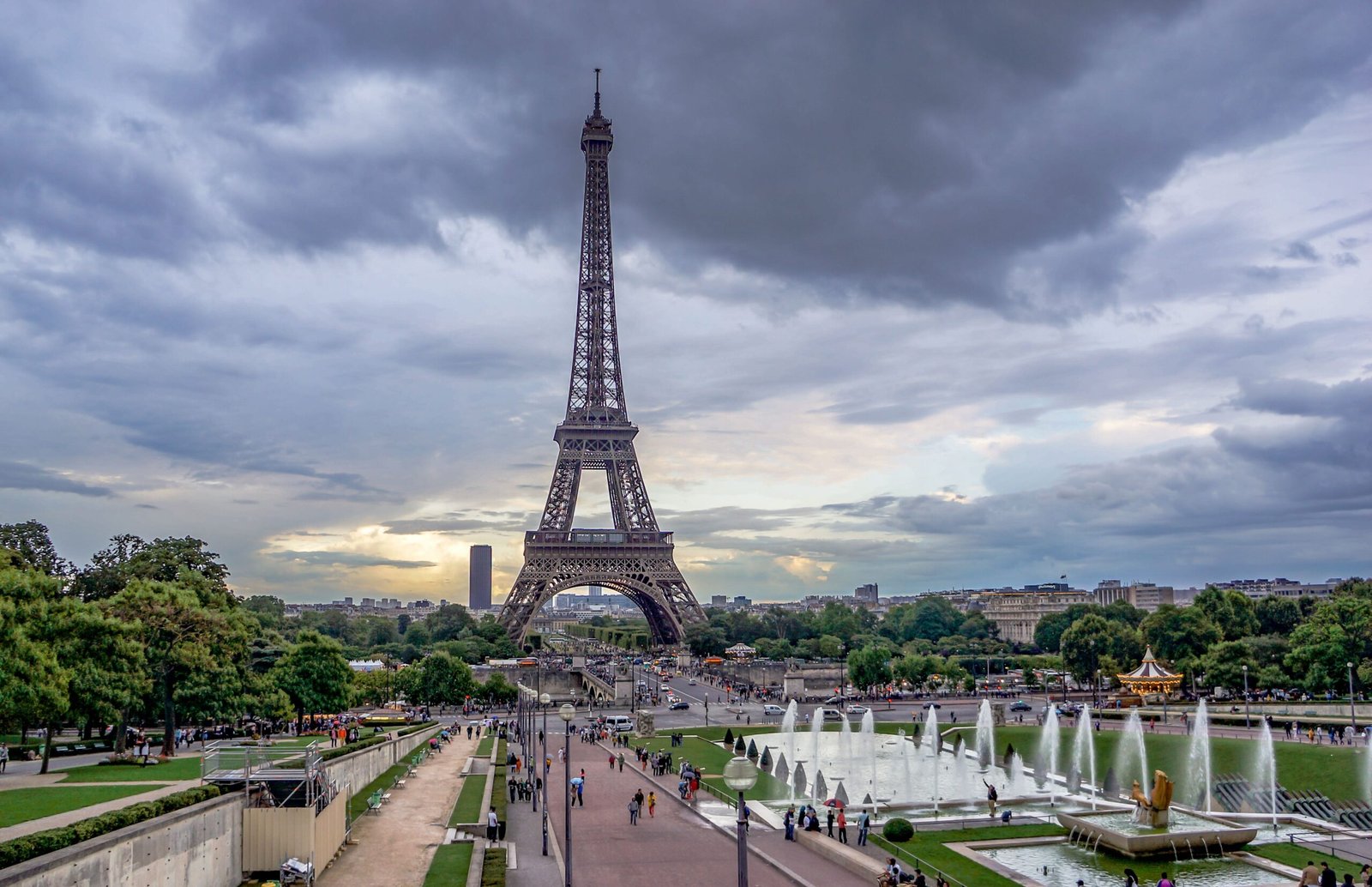 Eiffel Tower in Paris surrounded by greenery and fountains under a stormy sky.